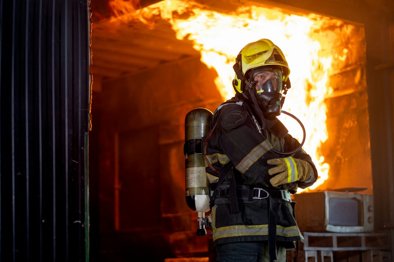 Firefighter man with protective and safety clothes stand with arm-crossed in front of fire