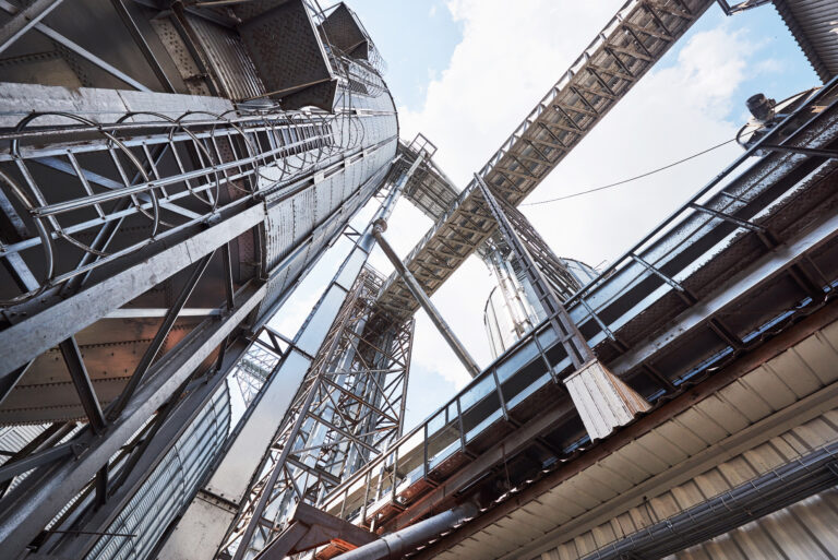 Upward view of steel silos with elevated catwalks and exposed support columns under industrial infrastructure.