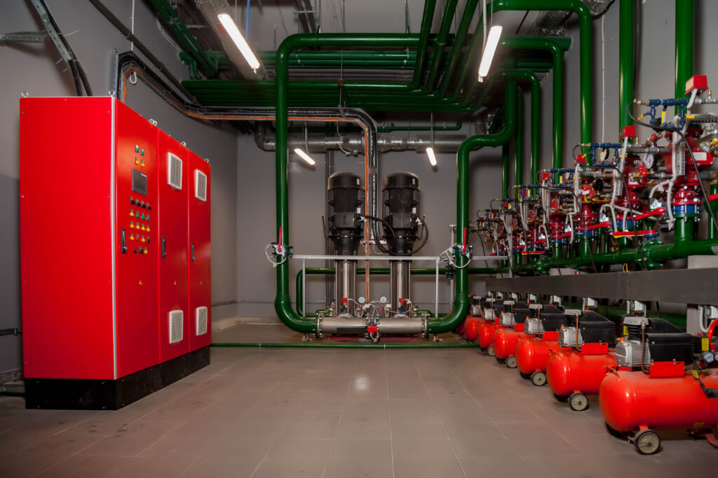 Fire pump room with red control panels, green pipes, water pumps, and pressure gauges.