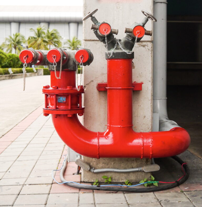 Outdoor red fire hydrant with dual valves and chained caps on a concrete base.